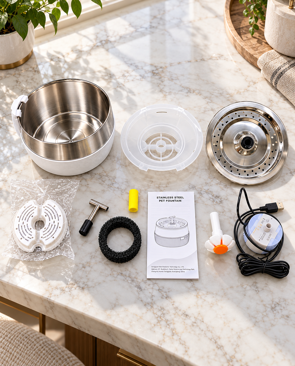 Disassembled stainless steel pet water fountain parts arranged on a premium marble table including water bowl, filter, pump, nozzle, and accessories